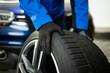 © zphoto83 - Worker changing tire of a car in a garage during daylight while wearing gloves and a blue jacket