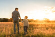 © kieferpix - Father and his son holding hands at sunset field. Dad leading son over summer nature outdoor. Family, trust, protecting, care, parenting concept
