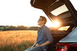 © kieferpix - Carefree smiling young man sitting in car hatchback trunk enjoying view of countryside sunset , travel, freedom concept