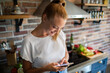 © Geber86 - Young woman holding smartphone in modern kitchen