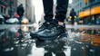 © SerPak - A person stands in a shallow puddle on a city street wearing sleek black athletic shoes. Raindrops create ripples in the water as traffic moves in the background, reflecting a typical rainy day in an