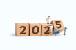 © Yunus Nugraha - Transitioning from 2024 to 2025 with wooden blocks and miniature people. new year 2025 concept.