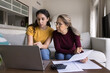 © fizkes - Focused Latin young daughter helping senior mother, showing how to use online financial e-bank application on laptop, paying bills on Internet, checking domestic expenses, budget, fees