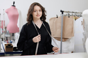 Wall Mural - Fashion tailor woman working on clothes in tailoring atelier. Young female designer smile in studio on work place