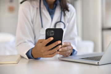 Close up female doctor using smartphone at workplace, access records, review medical histories, conduct virtual consultations with patients, provide advice, prescribe medication through telehealth app