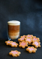 Wall Mural - Vertical shot of a glass of tasty coffee with a cookie on the dark background. Cup of coffee and Christmas cookies (cinnamon stars) on dark background. Delicious latte macchiato and cookies. Close up.