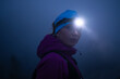 © .shock - female Hiker or triathlon trail runner with a headlamp on a trail in the mountain with fog at night
