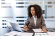 © Tetiana - Young african american female accountant, financial expert sitting in office at desk and working on laptop and documents