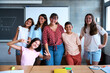 © CarlosBarquero - Portrait happy group of primary school student with teacher looking smiling at camera. Young diverse pre-teenagers people posing together for photo in classroom in front of blackboard. Back to school