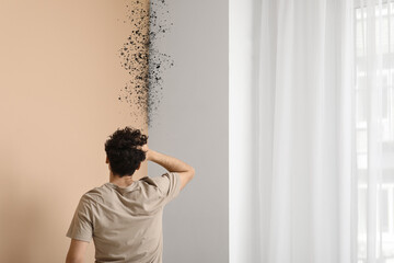 Shocked young man with mold on wall at home, back view