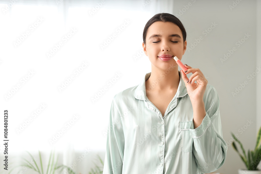 Beautiful young woman applying lip balm in bathroom