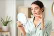 © Pixel-Shot - Young woman with mirror applying lip balm in bathroom
