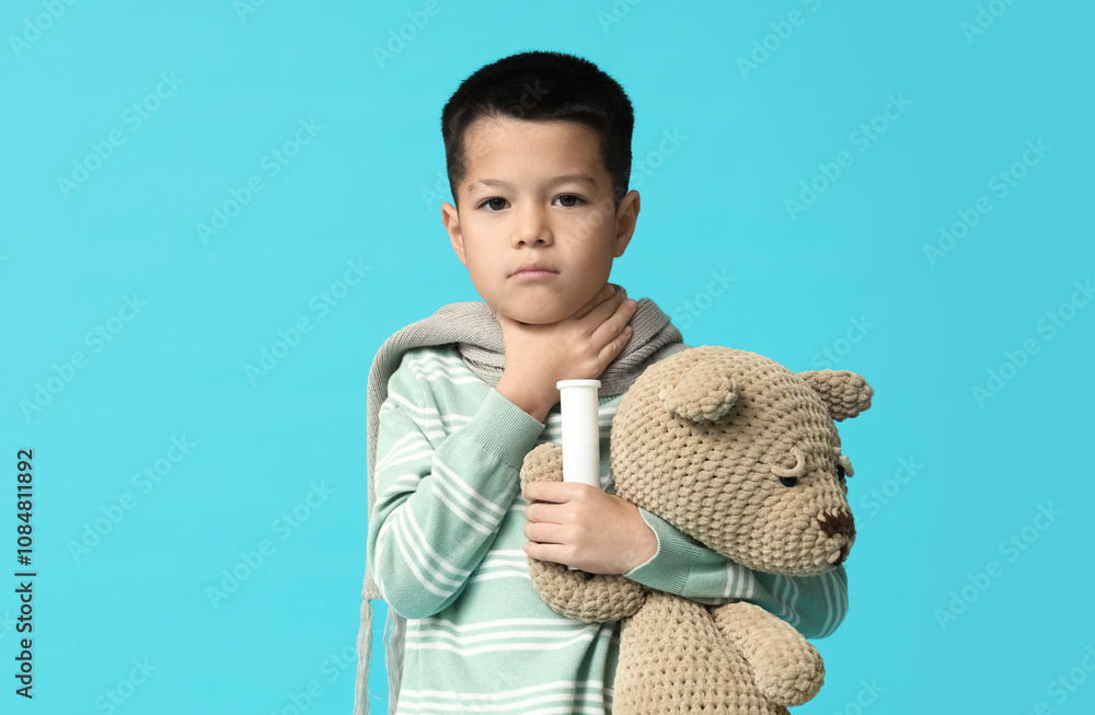 Ill little Asian boy with pills and toy bear on blue background