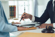 © Kritdanai - Legal Signing: A lawyer guides a client's hand as she signs an important document, symbolizing trust, legal counsel, and the finality of an agreement.