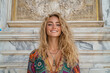 © Easy - A beautiful blonde girl standing in front of an Italian marble building is dressed in colorful and vibrant tribal patterns.