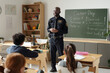 © pressmaster - Confident African American policeman in uniform standing in front of class of youthful kids and talking about his job and career