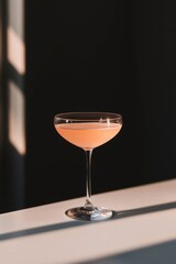 Elegant coupe glass with pink cocktail on bar counter with window light