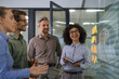 © ty - Businesspeople talking in their diverse team during a brainstorming session with sticky notes on glass wall in a modern office