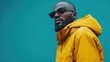 © imagineRbc - A fashionable man wearing a bright yellow jacket and trendy sunglasses stands confidently against a striking blue wall, embodying contemporary urban style and attitude