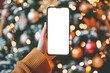© Marina Demidiuk - Close up black smartphone with blank screen in woman hand. Digital phone mock up. Christmas online shopping. Mobile phone with empty screen on background of Christmas tree lights. Tablet. Copy space