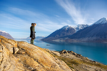 Wall Mural - man photographs the fjords and mountains of greenland, with schooner anchored in the deep blue water