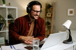 © djile - Happy businessman wearing headphones and working from his home office having a video conference on his laptop