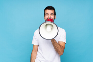 Wall Mural - Young man with beard  over isolated blue background shouting through a megaphone