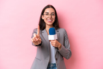 Wall Mural - Young caucasian tv presenter woman isolated on pink background showing and lifting a finger