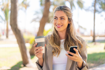 Canvas Print - Young pretty blonde Uruguayan woman at outdoors using mobile phone and holding a take away coffee