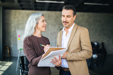 Fototapete - A woman and a man engage in a lively discussion in a contemporary office, with the woman taking notes on a notepad. Their expressions reflect collaboration and creativity.