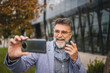 © Miljan Živković - Senior man explain something on video call in front modern building