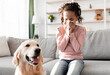 © Prostock-studio - Allergic Reaction To Fur. Sick black girl sneezing and sniffle holding paper tissue. Ill kid having rhinitis suffering from running nose caused by her pet dog, sitting on sofa at home, free space