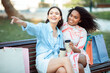 © Prostock-studio - Two friends relax on a park bench, sharing laughter and conversation after a day of shopping. They sip coffee and enjoy each other's company while surrounded by shopping bags.