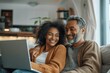 © zong - Middle aged couple smiling while using laptop on modern living room sofa shopping online at home