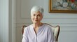 © Tati - Elderly woman with short white hair, sitting on chair, smiling in well-lit room framed artwork background