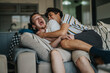 © qunica.com - Two friends share a joyful and playful moment on the couch, laughing and embracing each other in a casual home setting.