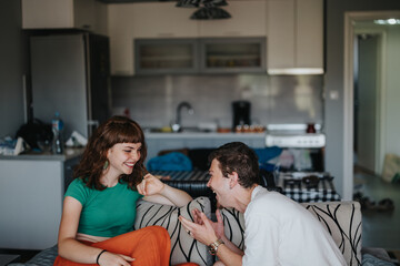 Wall Mural - A cheerful moment between two friends laughing and enjoying a relaxed time in a comfortable home setting. Capturing joy, friendship, and the simplicity of shared moments.