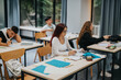 © qunica.com - Students engage in learning activities in a contemporary classroom filled with natural light. Diversity and concentration highlight the academic environment, emphasizing education and collaboration.