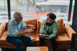 © qunica.com - An elderly mentor providing guidance to a young student seated on a cozy sofa. The discussion embodies wisdom sharing and attentive listening in a quiet study environment.