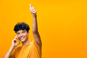 Wall Mural - cheerful young man talking on the phone with a thumbs up gesture, bright yellow background, expressing positivity and joy, casual attire, engaging in conversation, happiness captured in vibrant colors