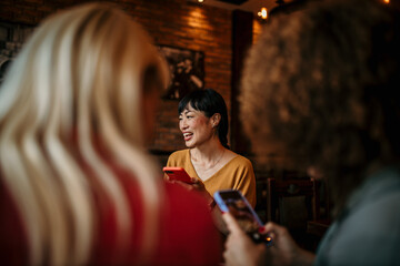 Wall Mural - Photo of cheerful friends during a dinner party in an indoors bistro, having fun while taking photos and selfies