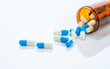 © Artinun - Prescription antibiotic capsules spilling from amber bottle onto a white background. Blue and white capsule pills. Ideal for healthcare, pharmaceutical treatments, and medical medication industries.