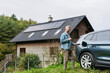 © Halfpoint - Man charging electric car in front of his house, plugging the charger into the charging port. House with solar panel system on roof behind him.