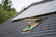 © Halfpoint - Man looking from skylight, roof window with solar panels above him. Sustainable lifestyle and green household.