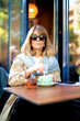 © sepy - Attractive blond haired woman sitting at a table outside a cafe and drinking capuccino