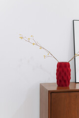 Poster - Red vase with branches on wooden cabinet in minimalist room