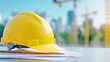 © Irina Tch - Close-up of a yellow hard hat resting on blueprints with a city construction site in the background, symbolizing safety and planning.