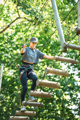 Wall Mural - a young woman skillfully navigates a ropes course, showcasing her adventurous spirit in a lush setti