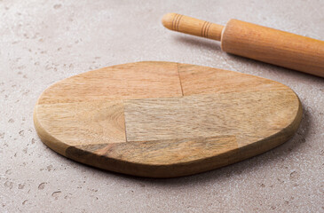 Empty wooden cutting board and a wooden rolling pin on a beige stone table, mockup for design