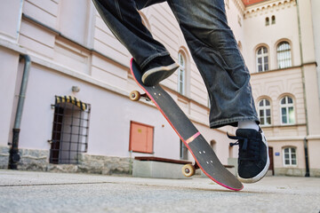 Skateboarder doing ollie trick at urban street. Close up of skater wearing baggy jeans balancing on skateboard. Concept of youth subculture